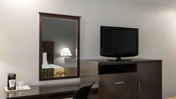 A hotel room with a dark wooden desk, a television, a mirror, and a bed with a yellow patterned bedspread.