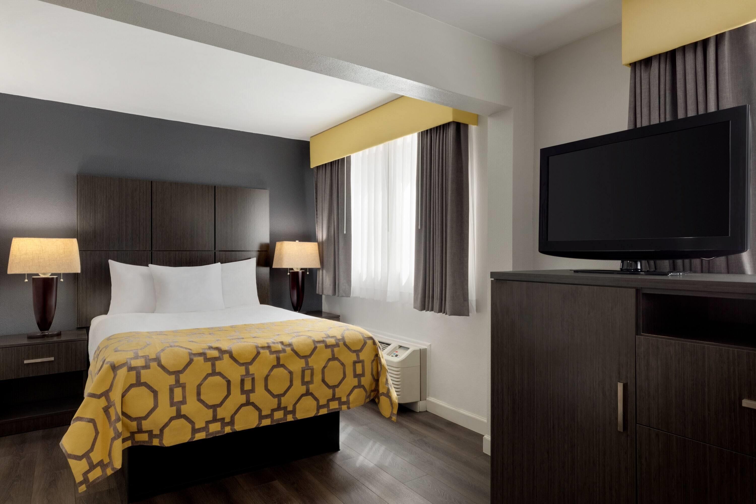 A hotel room with a bed, two bedside lamps, a television, and a wardrobe.