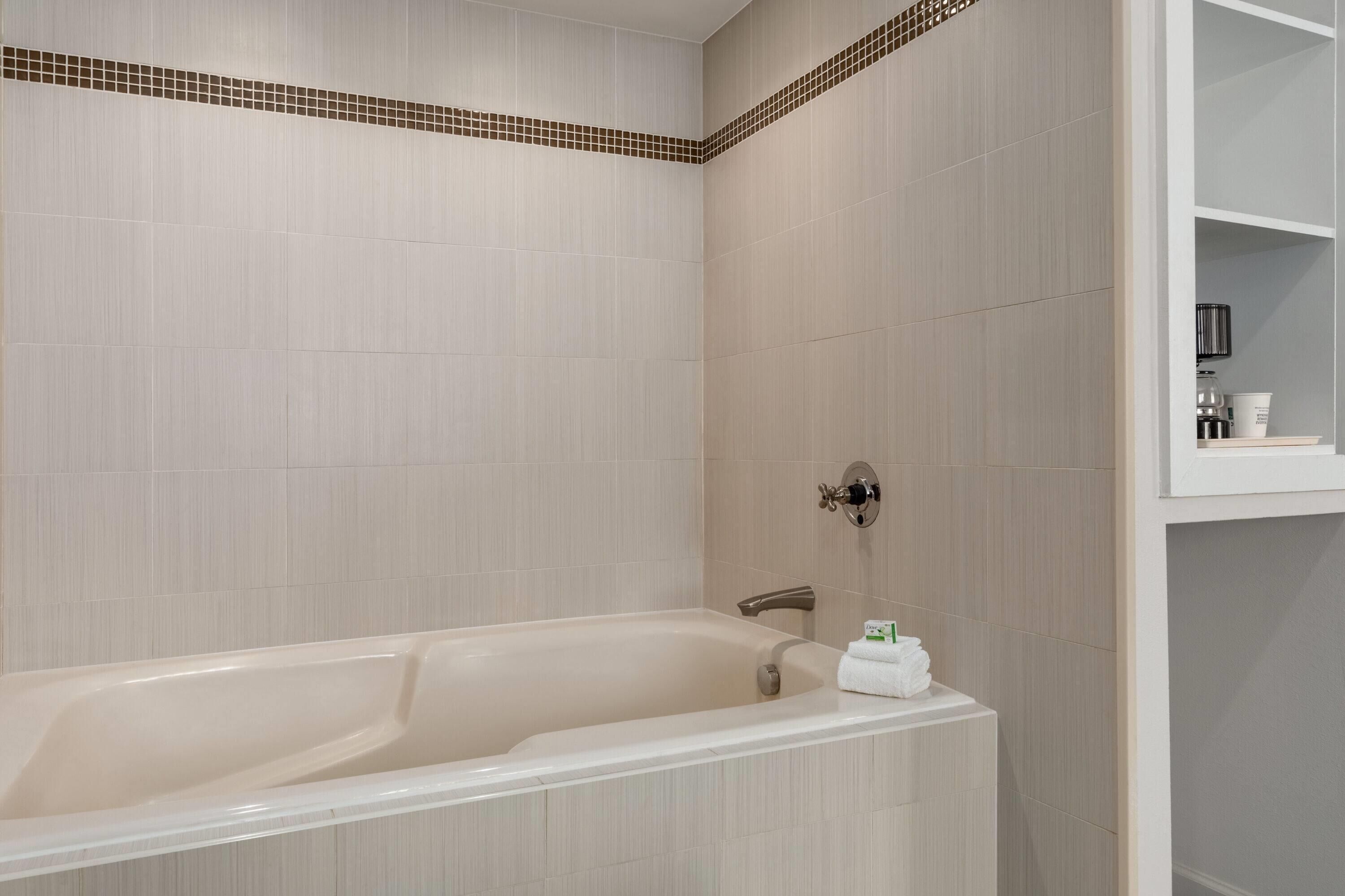 Un baño moderno con bañera, zona de ducha y un estante blanco con artículos de aseo.
