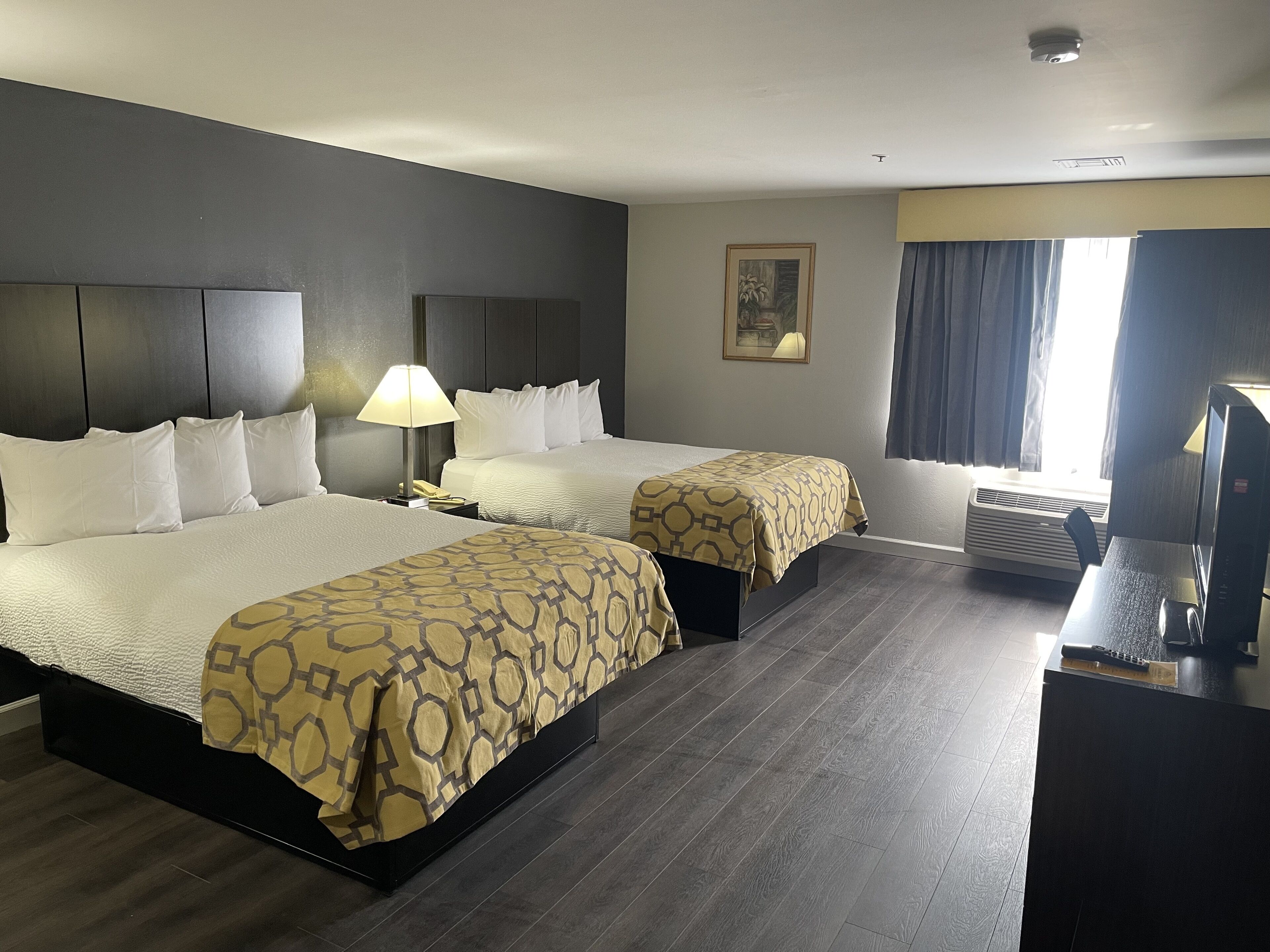 A hotel room with two beds, a desk, a lamp, a telephone, and a painting on the wall.