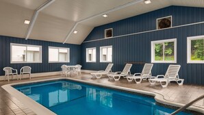 Ein beheiztes Hallenbad mit klarem, blauem Wasser, umgeben von weißen Liegestühlen und Tischen.