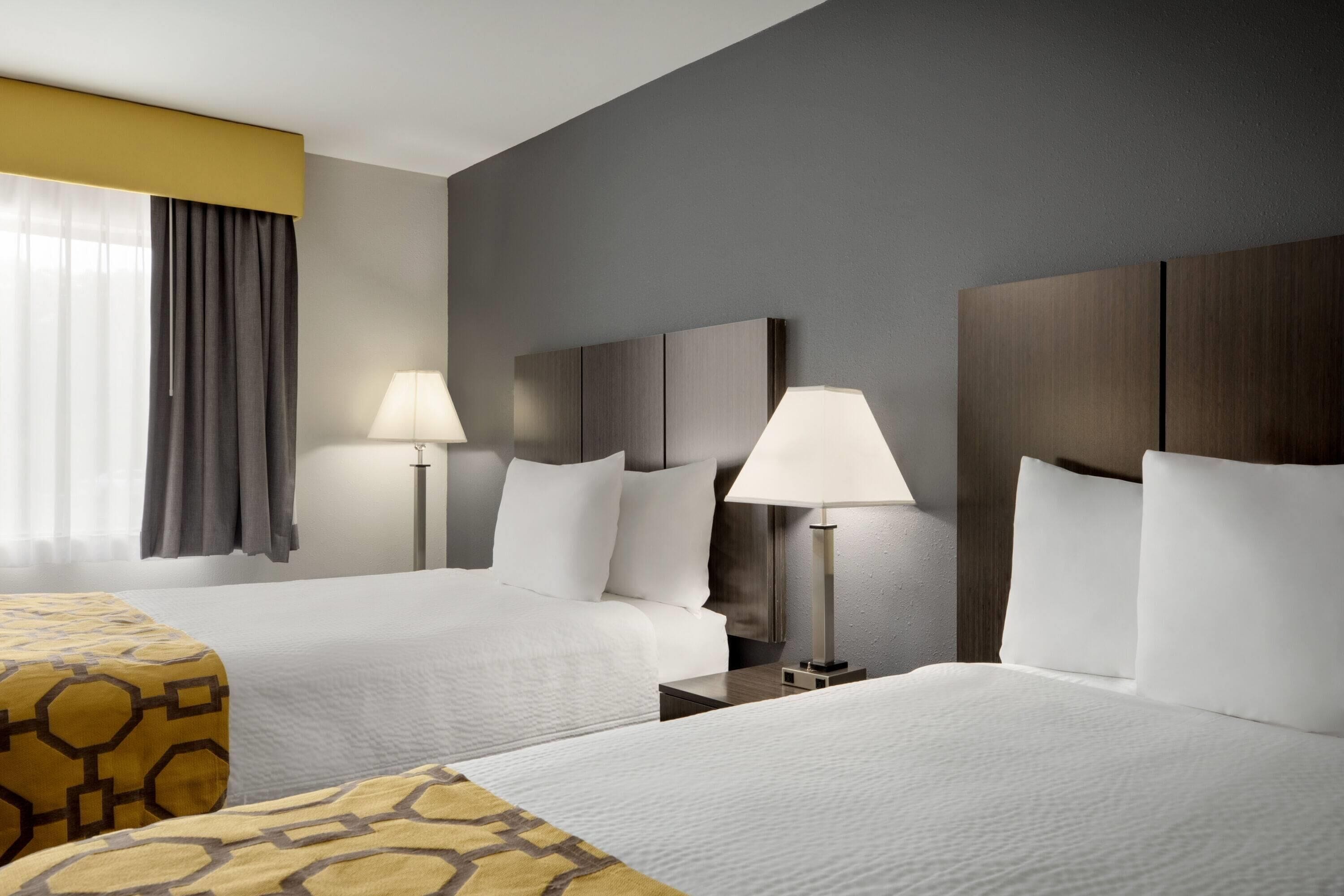 A hotel room with two beds, a large window with curtains, and two bedside lamps.