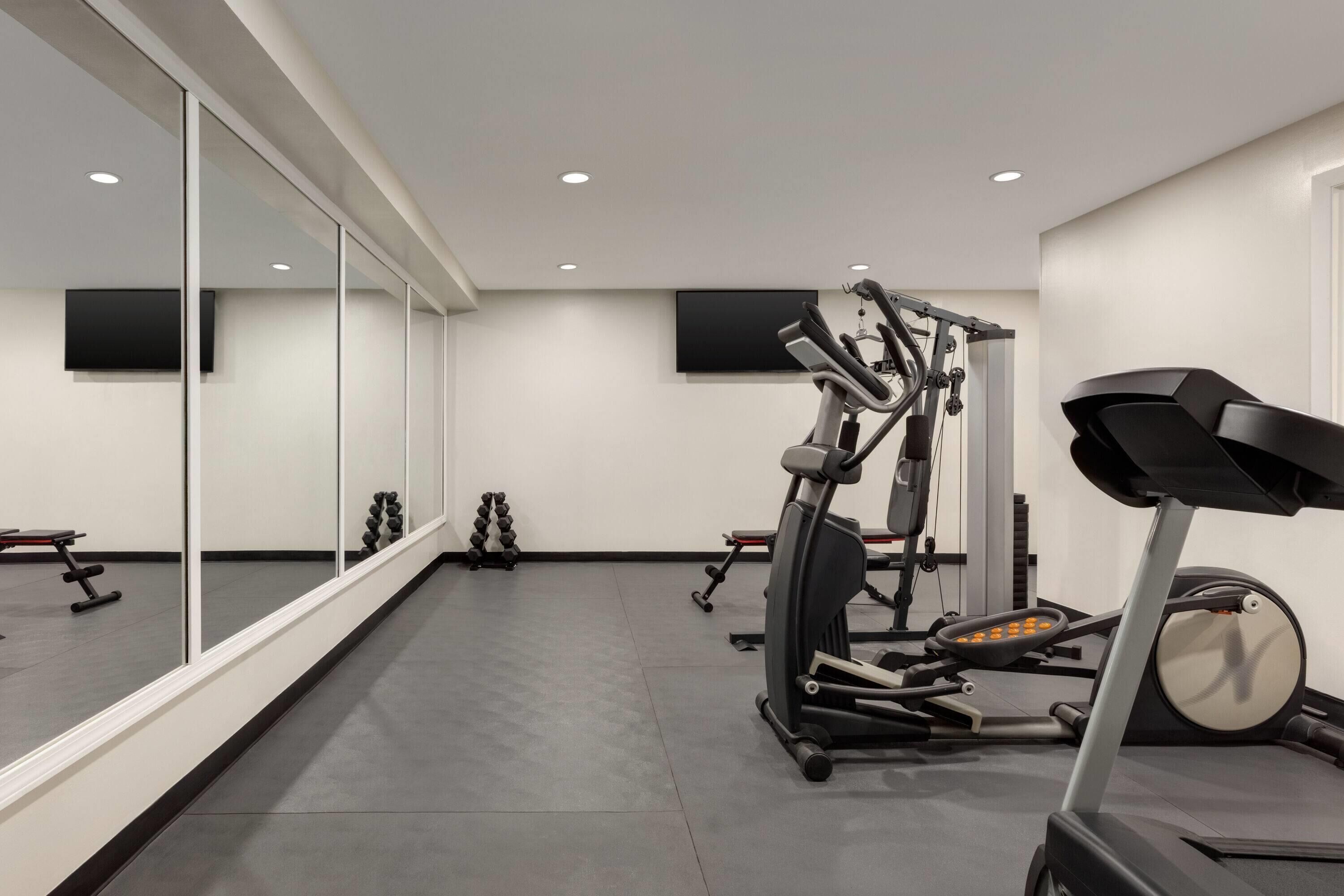 A modern gym with exercise equipment, large mirrors, and a flat-screen TV on the wall.