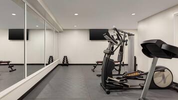 A modern gym with exercise equipment, large mirrors, and a flat-screen TV on the wall.