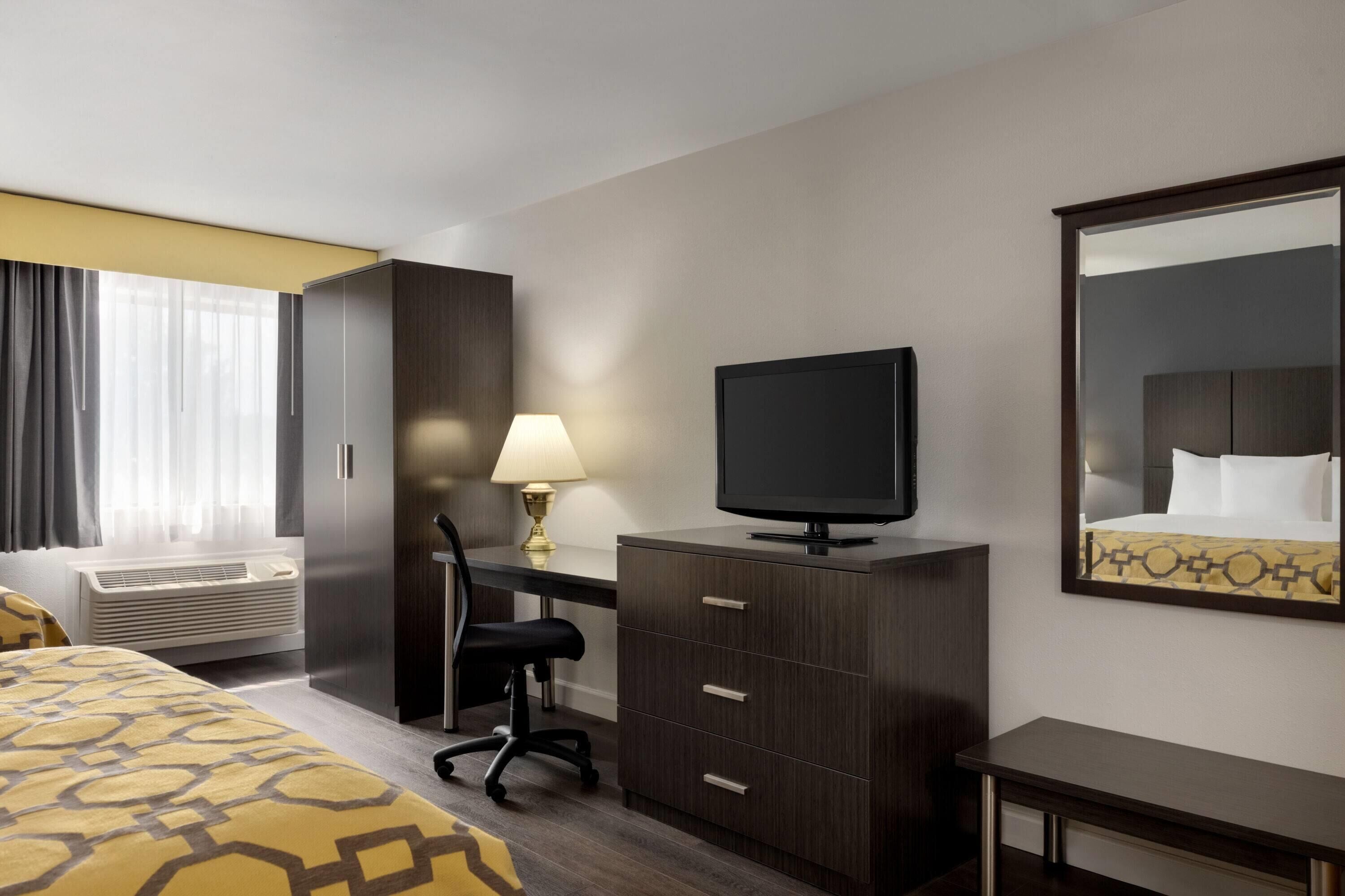 Habitación de hotel con cama, escritorio, silla, televisor, armario y espejo.