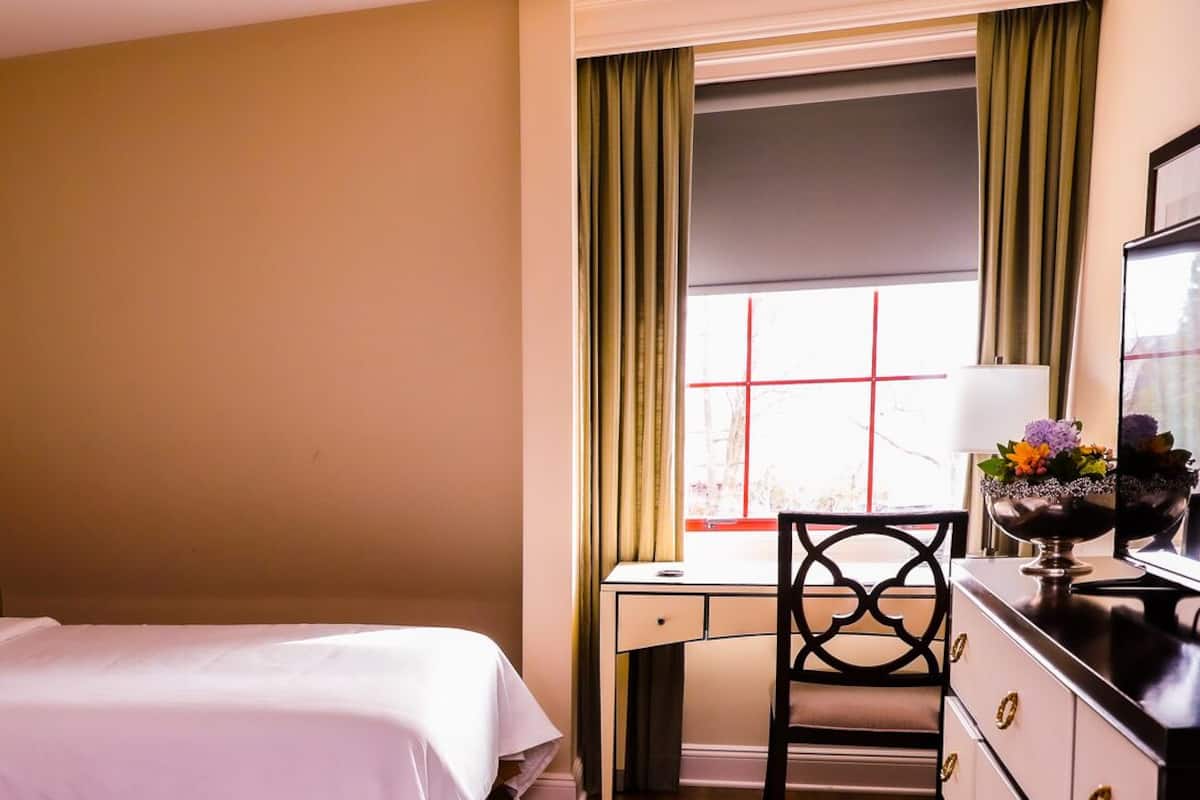 A hotel room with a bed, a desk, a chair, a dresser, and a window with curtains.
