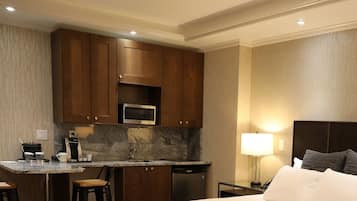 Une chambre d’hôtel équipée d’une kitchenette, d’un lit, d’une table de chevet avec une lampe et d’une chaise.