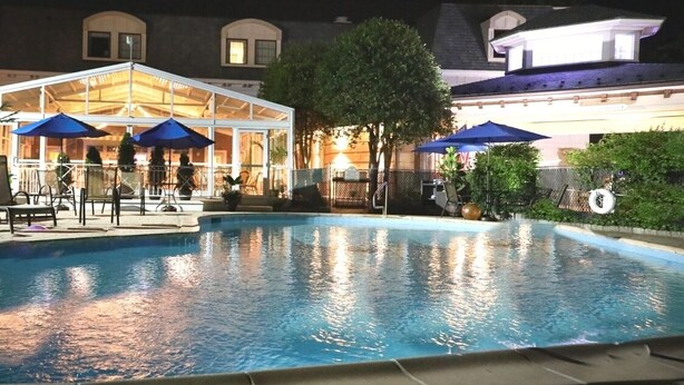 A swimming pool with lounge chairs and umbrellas, surrounded by a covered patio area.