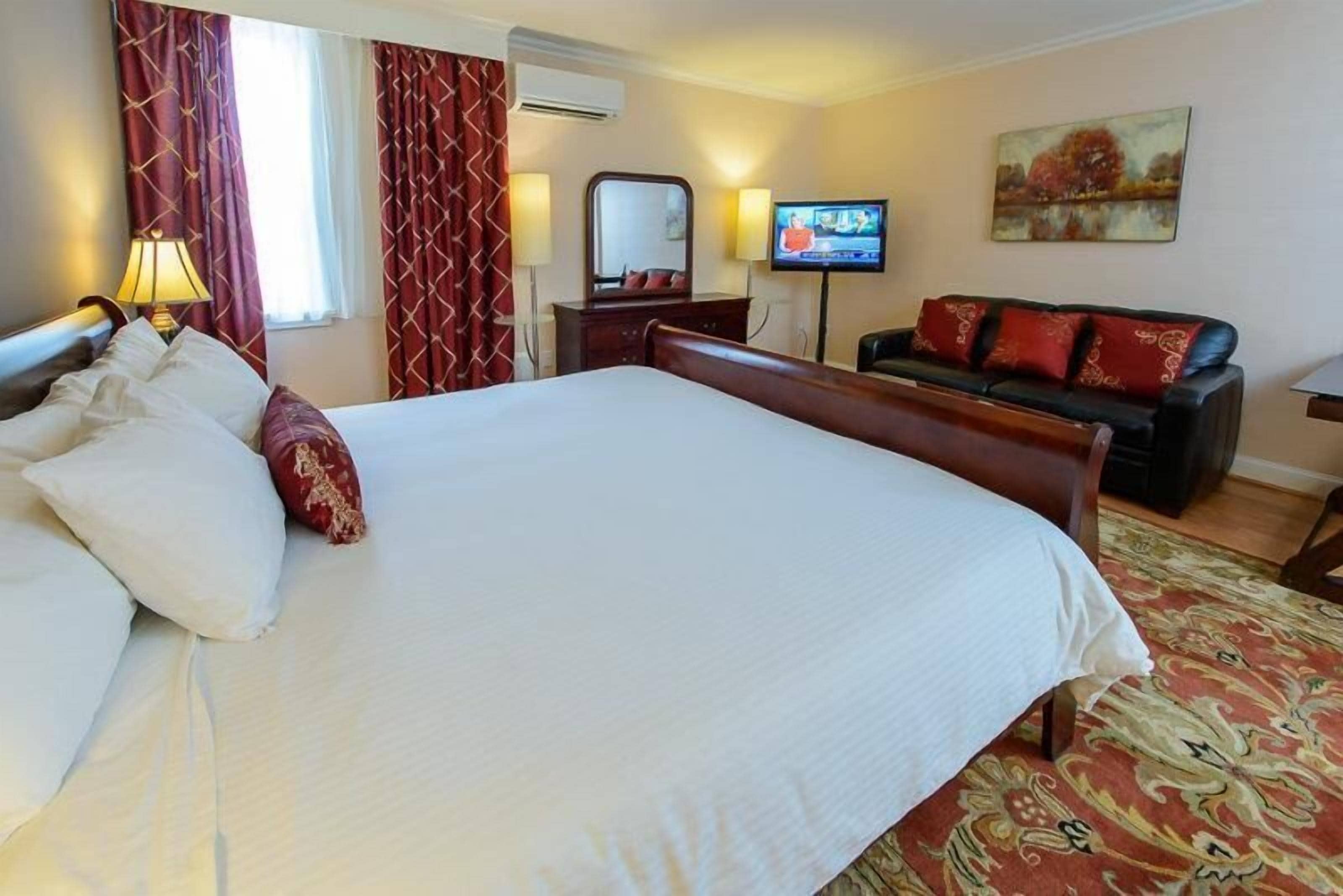 Una habitación de hotel con una cama grande, un sofá, un televisor y un cuadro en la pared.