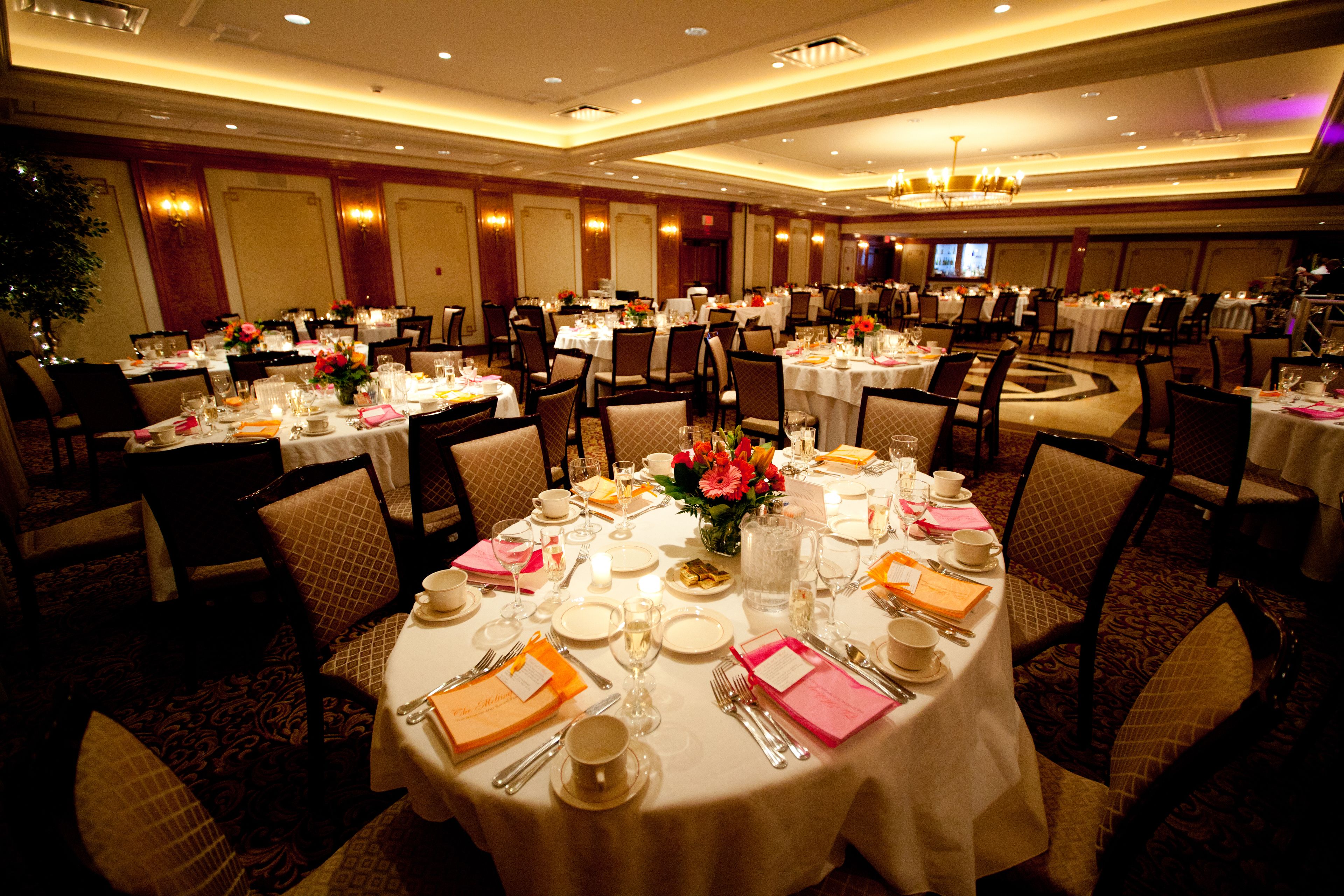 Un salón de banquetes con mesas redondas dispuestas para comer, cada una con mantel blanco, sillas y centros de mesa.