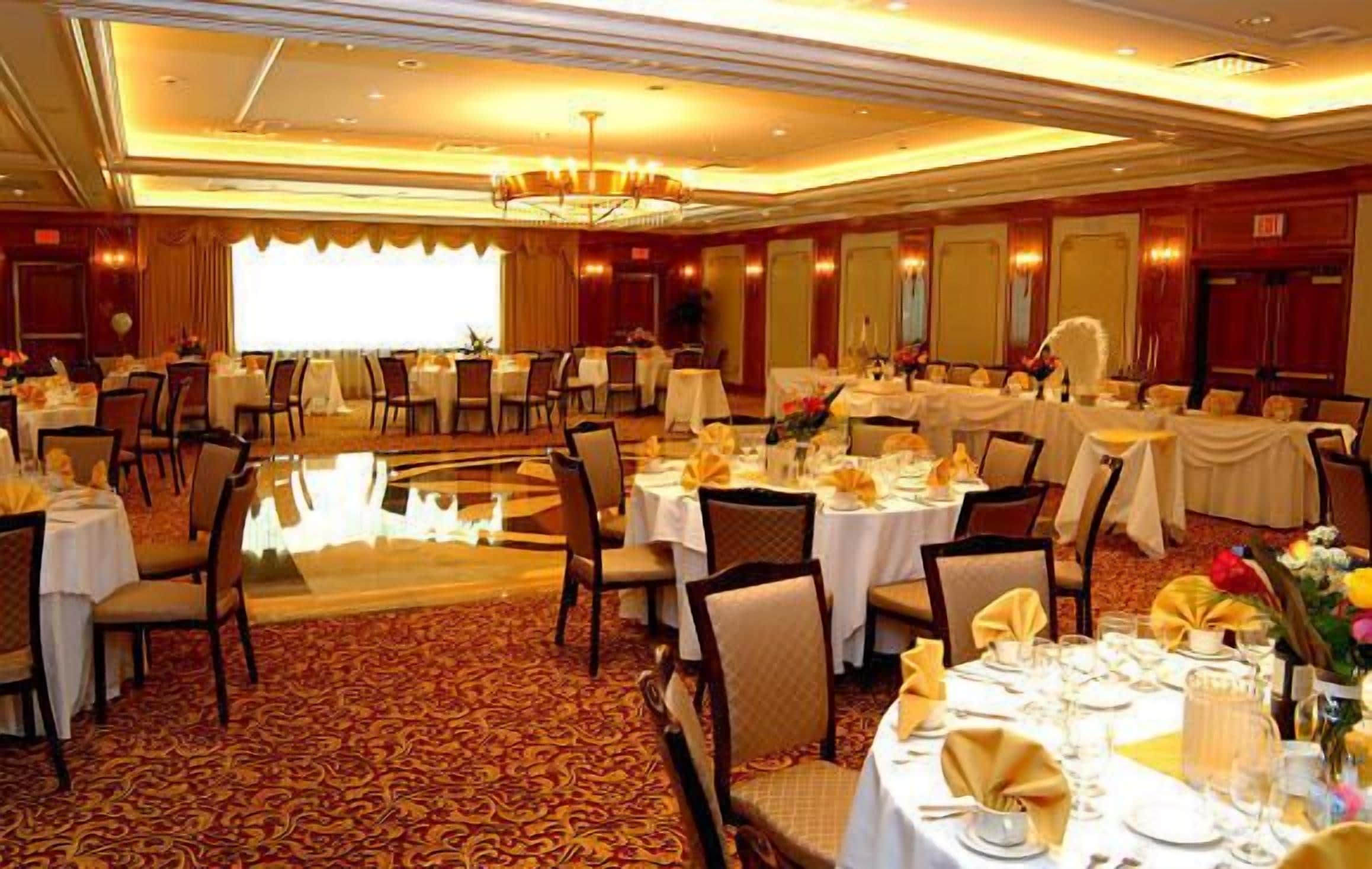 Een feestzaal met ronde tafels gedekt voor een diner, een kroonluchter en een vloerbedekking.