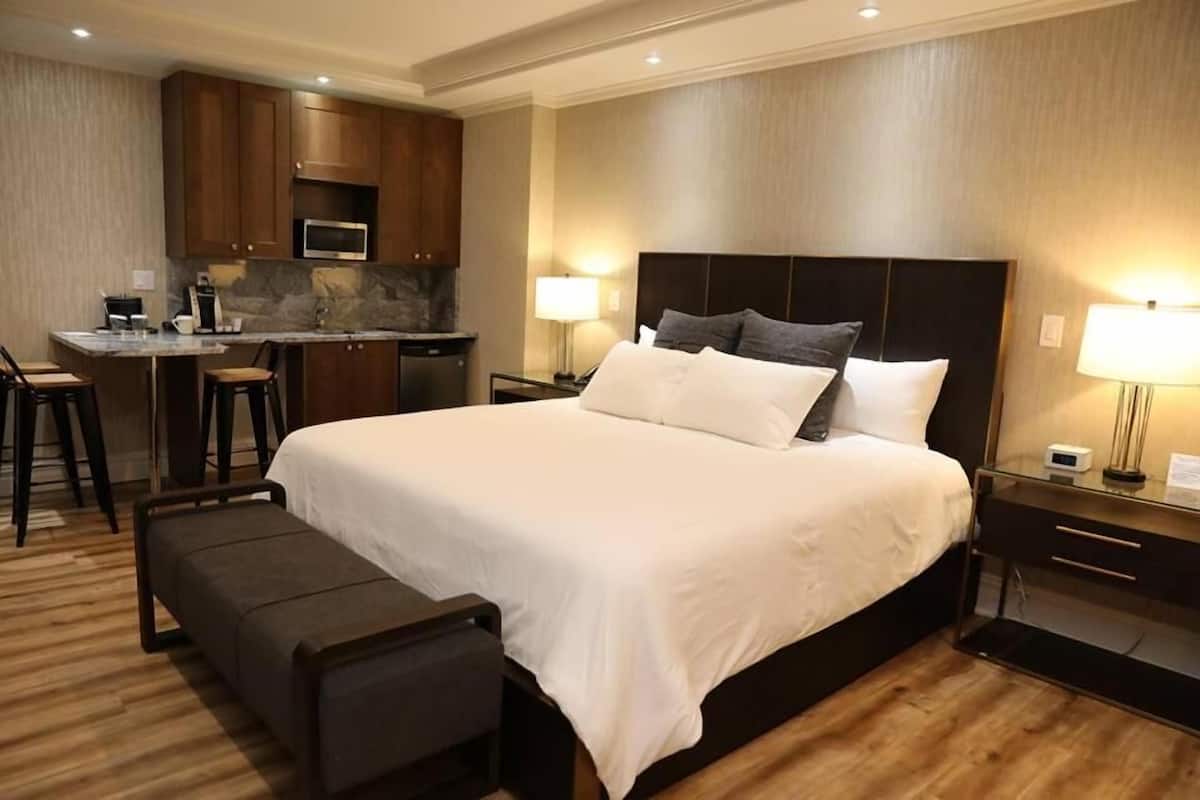 A hotel room with a large bed, a desk with a chair, a microwave, and a small kitchenette.