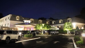 A hotel with a central entrance, multiple parking spaces, and a well-lit driveway.
