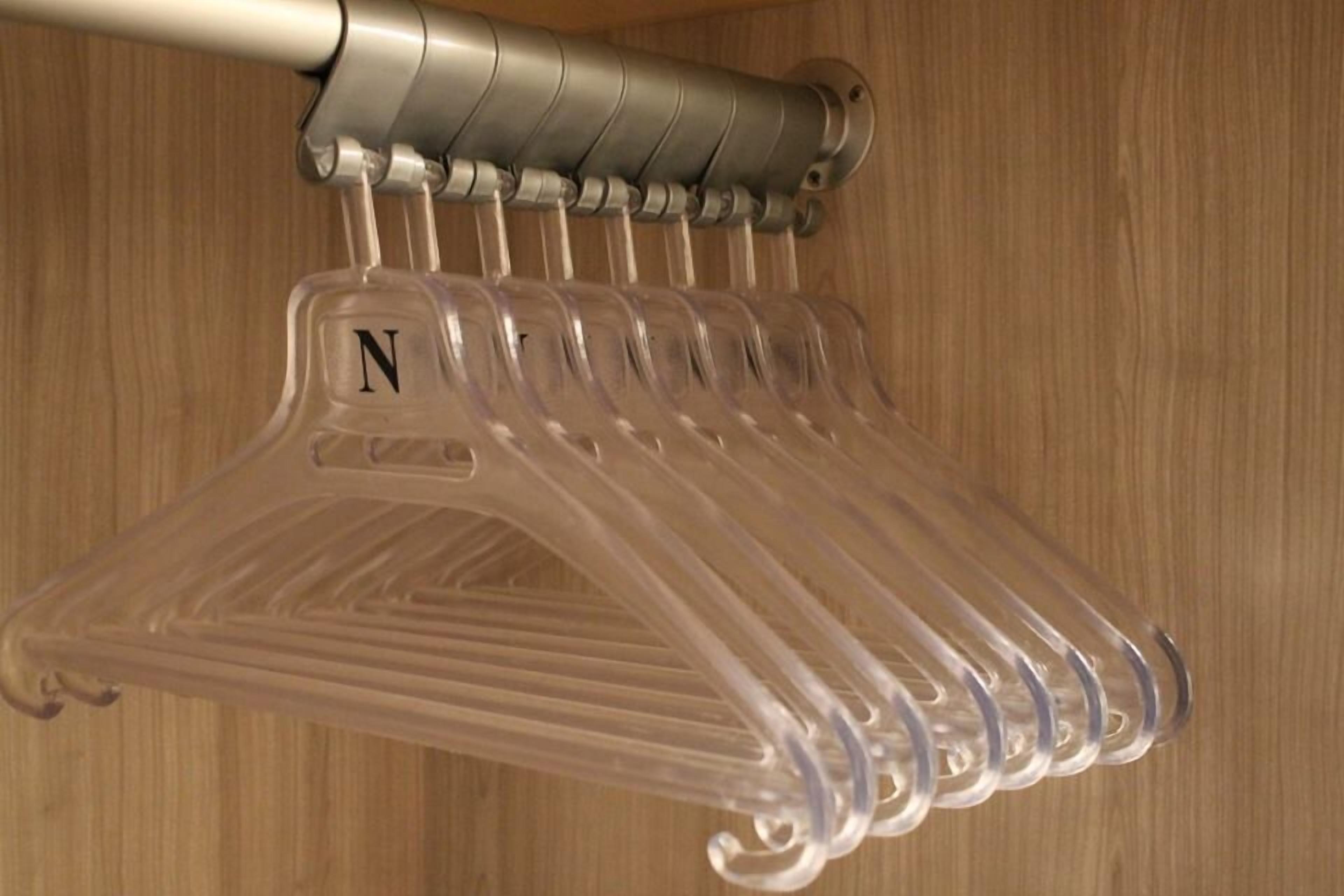 A clear plastic hanger rack with a letter 'N' on one of the hangers, mounted on a wall with a wooden panel background.