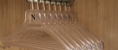 A clear plastic hanger rack with a letter 'N' on one of the hangers, mounted on a wall with a wooden panel background.