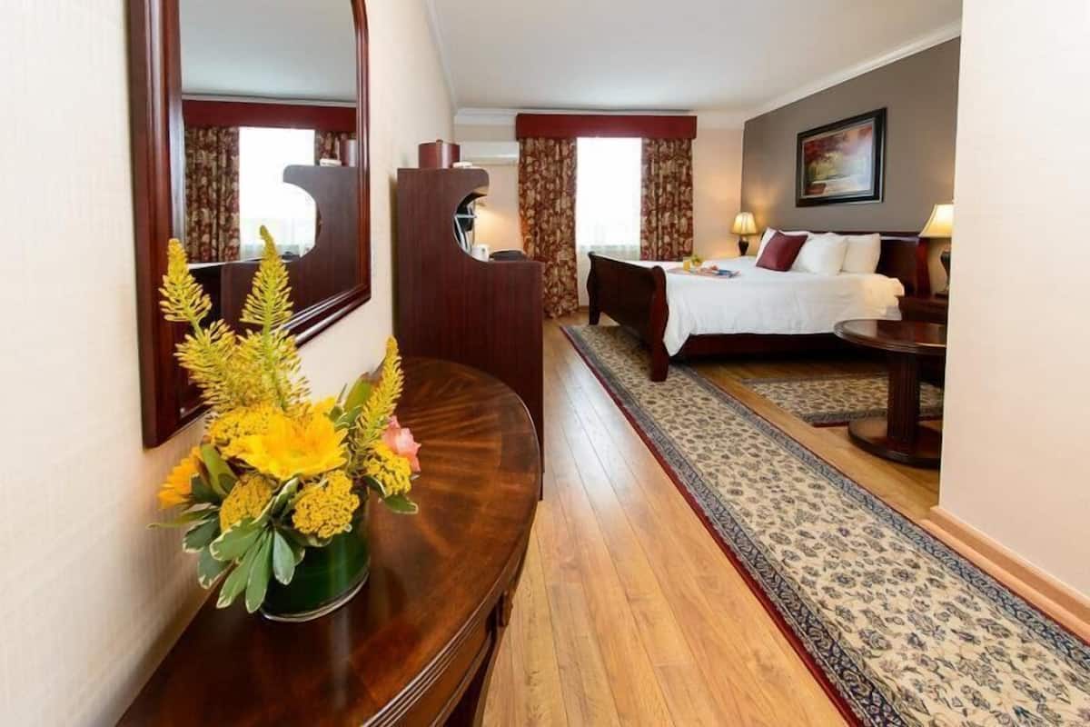 A hotel room with a bed, a desk with a mirror, a vase of flowers, and a patterned rug.