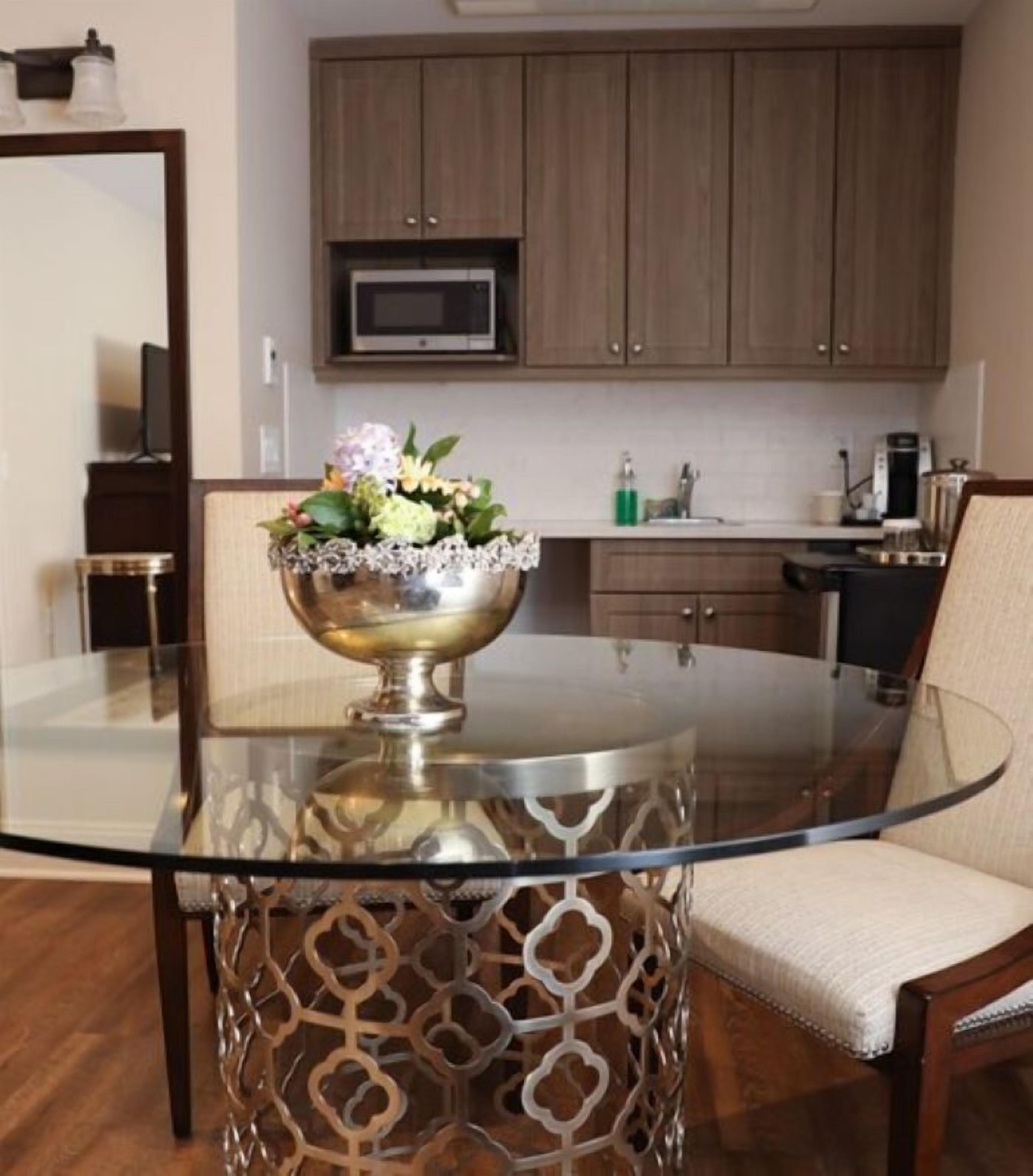 Uma cozinha moderna com armários de madeira, micro-ondas e uma mesa de jantar de vidro com um recipiente decorativo.