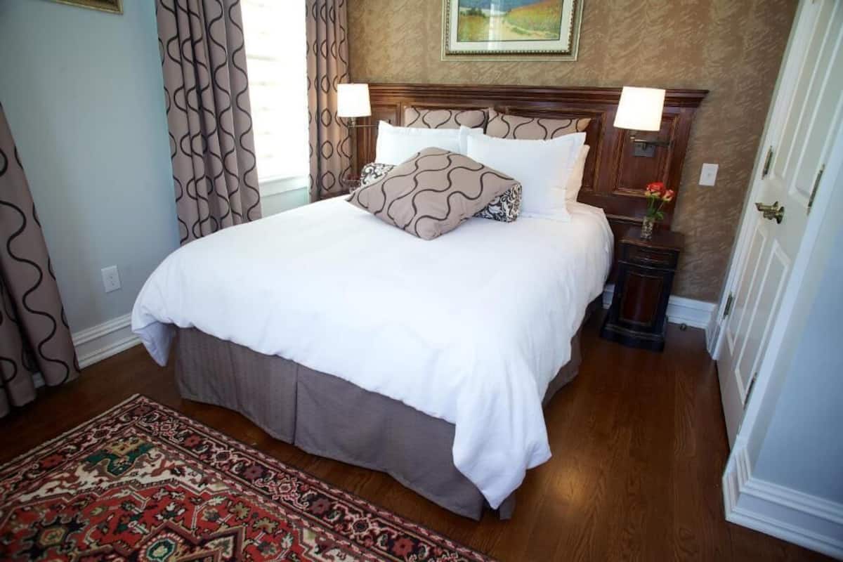 A neatly made bed with a patterned throw, a wooden headboard, and a bedside table with a lamp and vase of flowers.