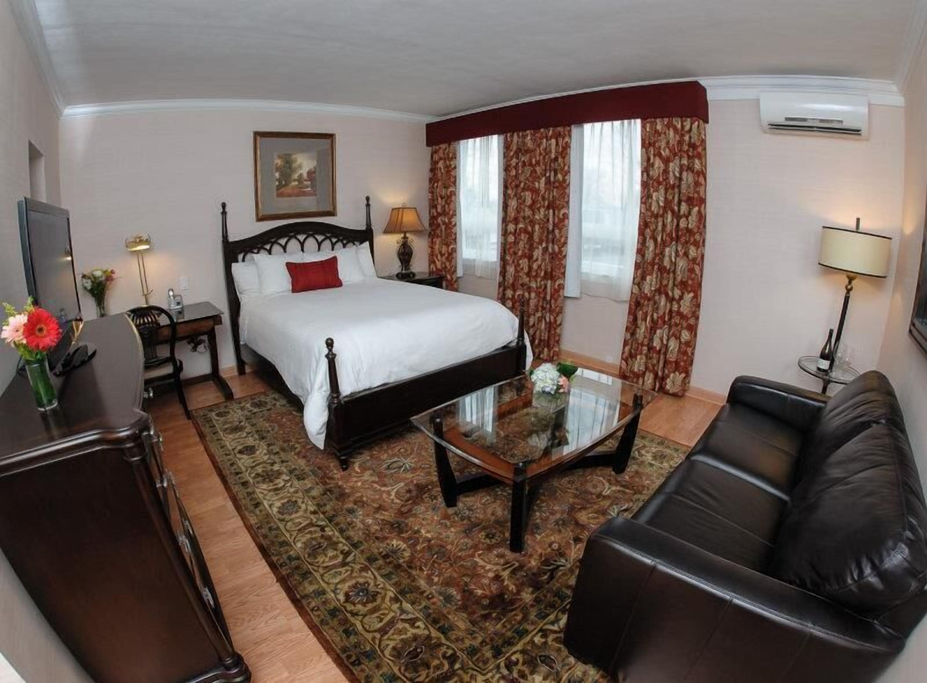 A hotel room with a bed, a glass coffee table, a leather sofa, a desk, and a chair.