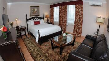 A hotel room with a bed, a glass coffee table, a leather sofa, a desk, and a chair.