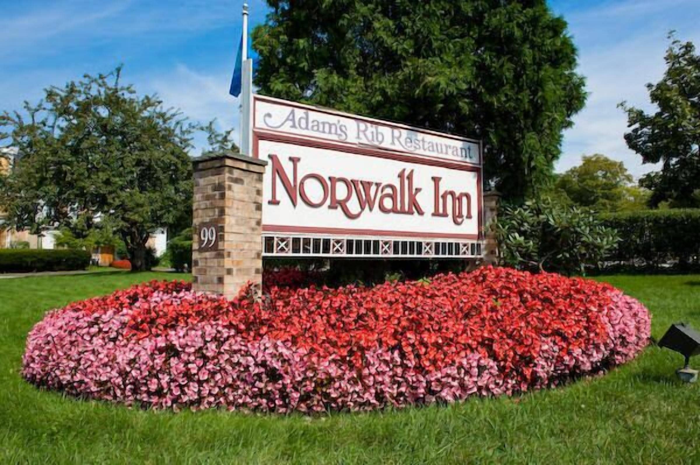 A Norwalk Inn sign with a red flower bed in front.