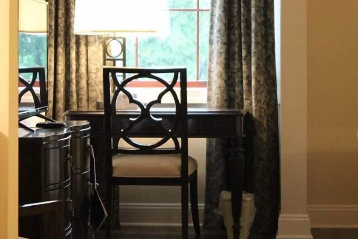 A room with a dining table, two chairs, a lamp, and a window with curtains.