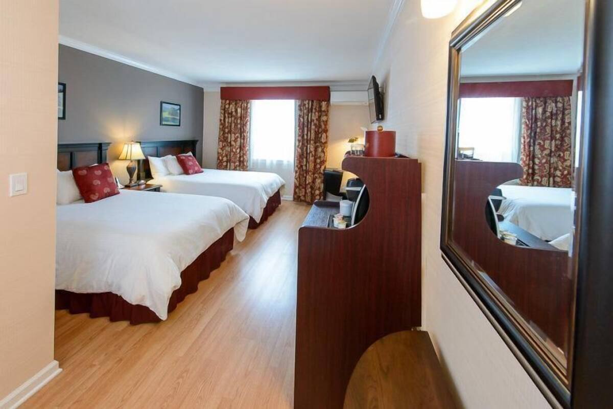 A hotel room with two beds, a desk, a mirror, and a television.