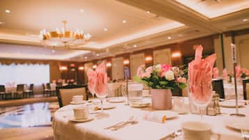 A banquet table set with white tablecloths, pink napkins, and a vase of flowers.