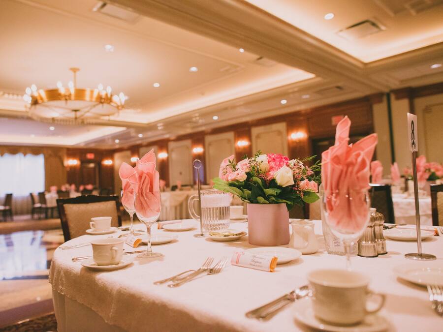 A banquet table set with white tablecloths, pink napkins, and a vase of flowers.