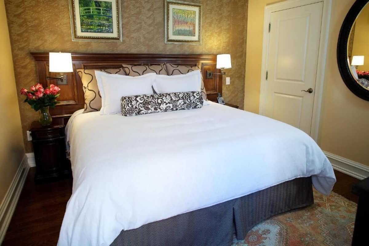 A neatly made bed with white linens and decorative pillows, a wooden headboard, and two framed artworks on the wall.