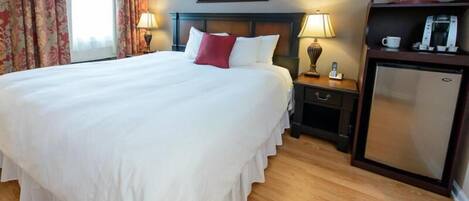 A hotel room with a large bed, bedside lamps, a small refrigerator, and a painting on the wall.