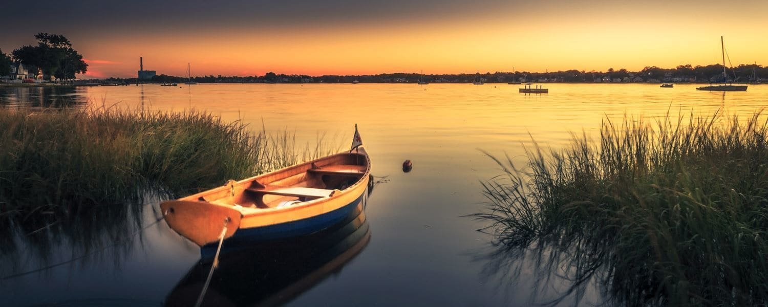 A calm river with a small rowboat tied to the shore, surrounded by tall grasses.