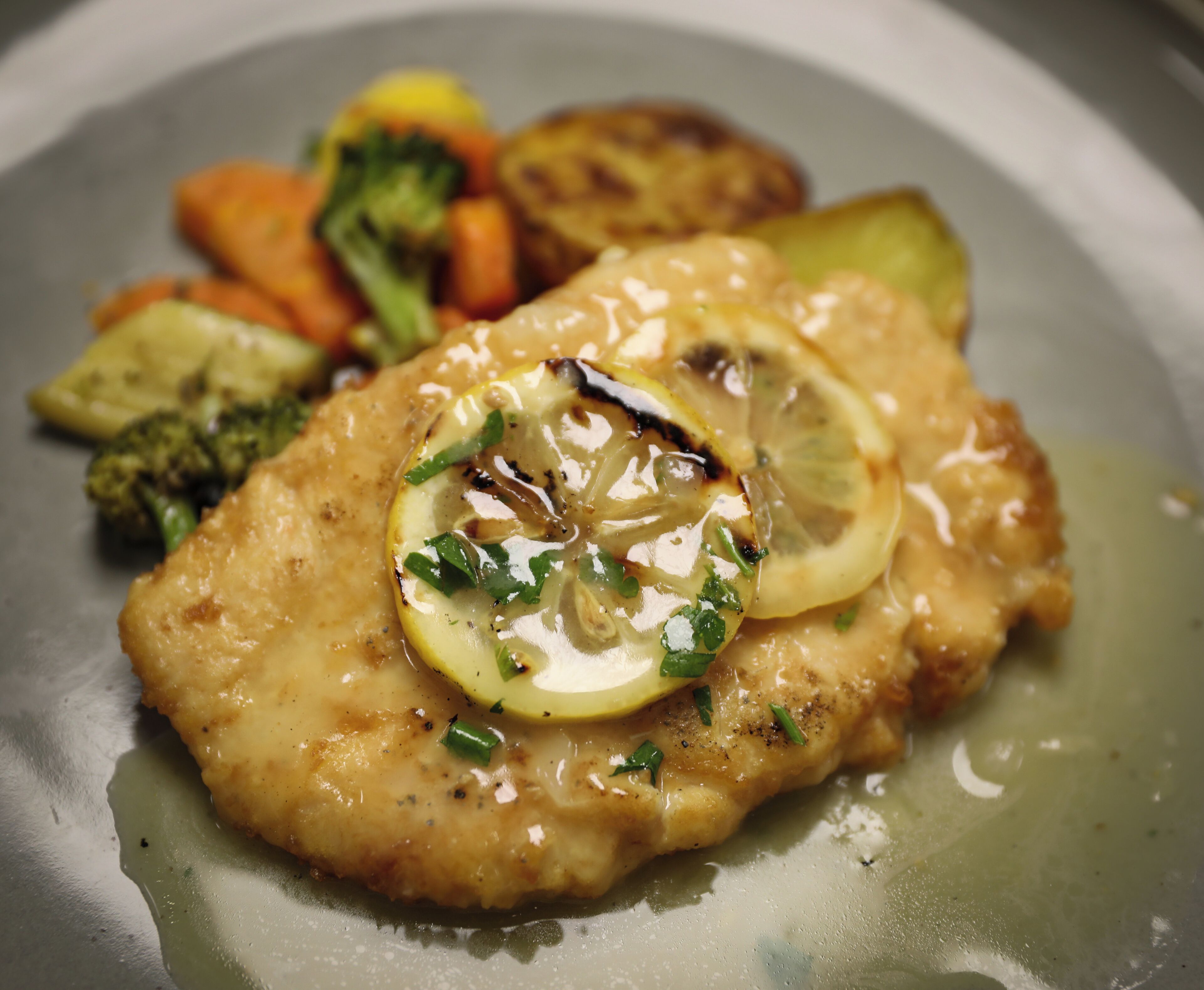 Un plat composé d’une portion de poulet, de légumes et d’une tranche de citron en garniture.