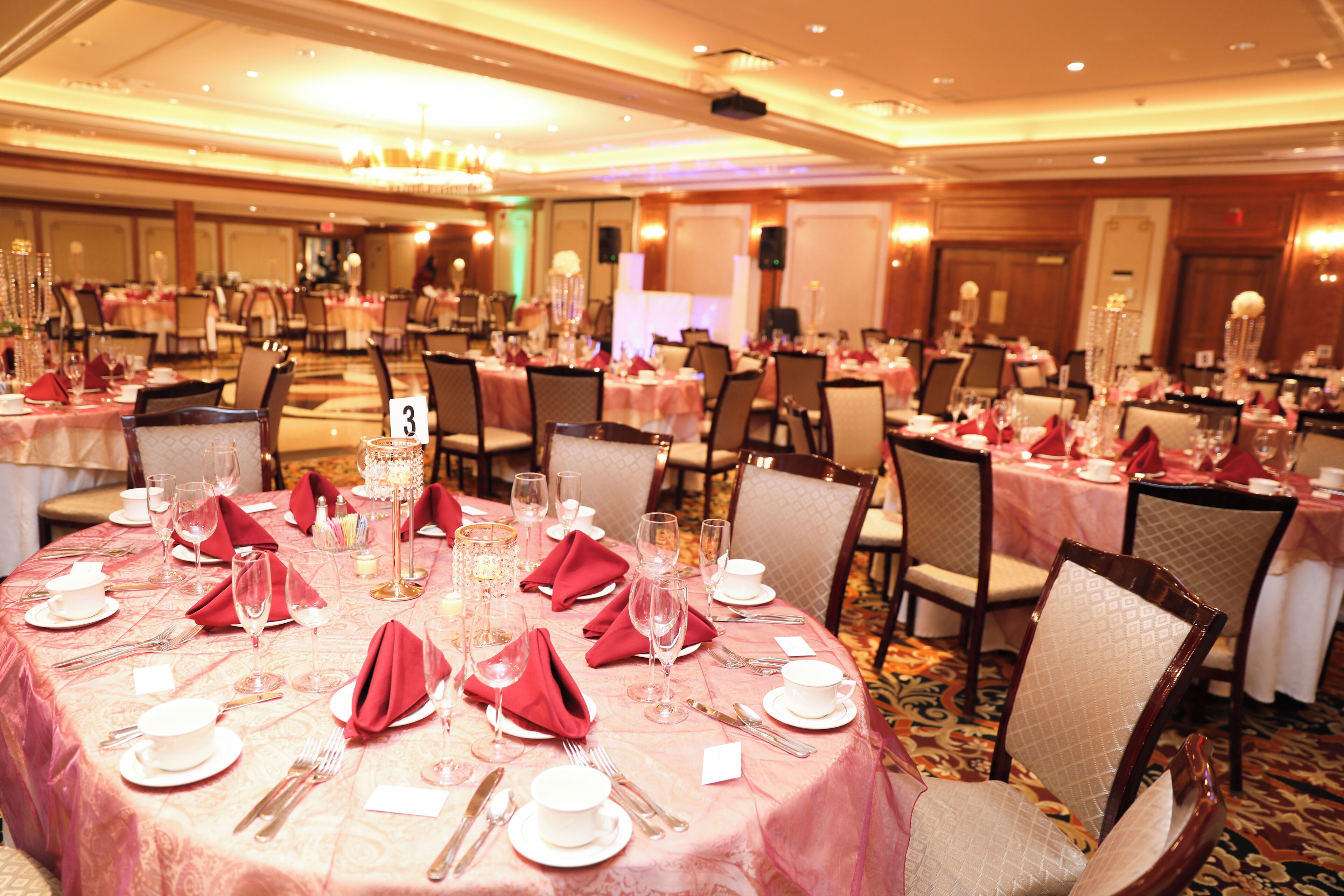 Un salón de banquetes con mesas redondas dispuestas para comer, posavasos numerados y sillas con respaldo acolchado.