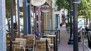 Outdoor seating with wooden chairs and tables, a sign for Bacchus, and a street with parked cars.