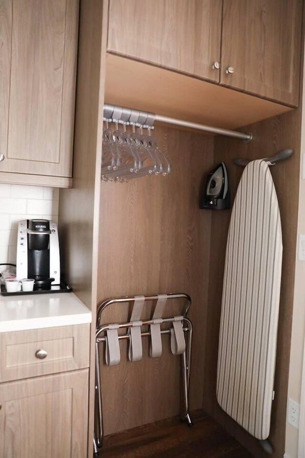 A compact kitchen with a coffee maker, a drying rack, and an ironing board.