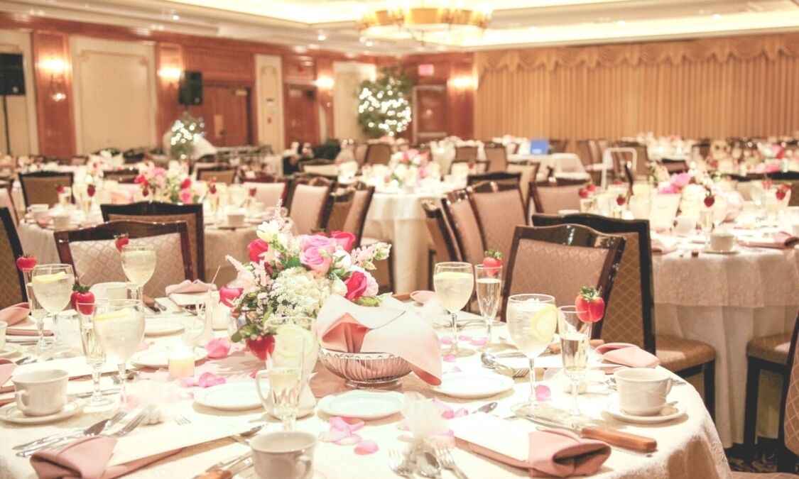 A banquet hall with round tables set for a formal event, featuring floral centerpieces and white tablecloths.