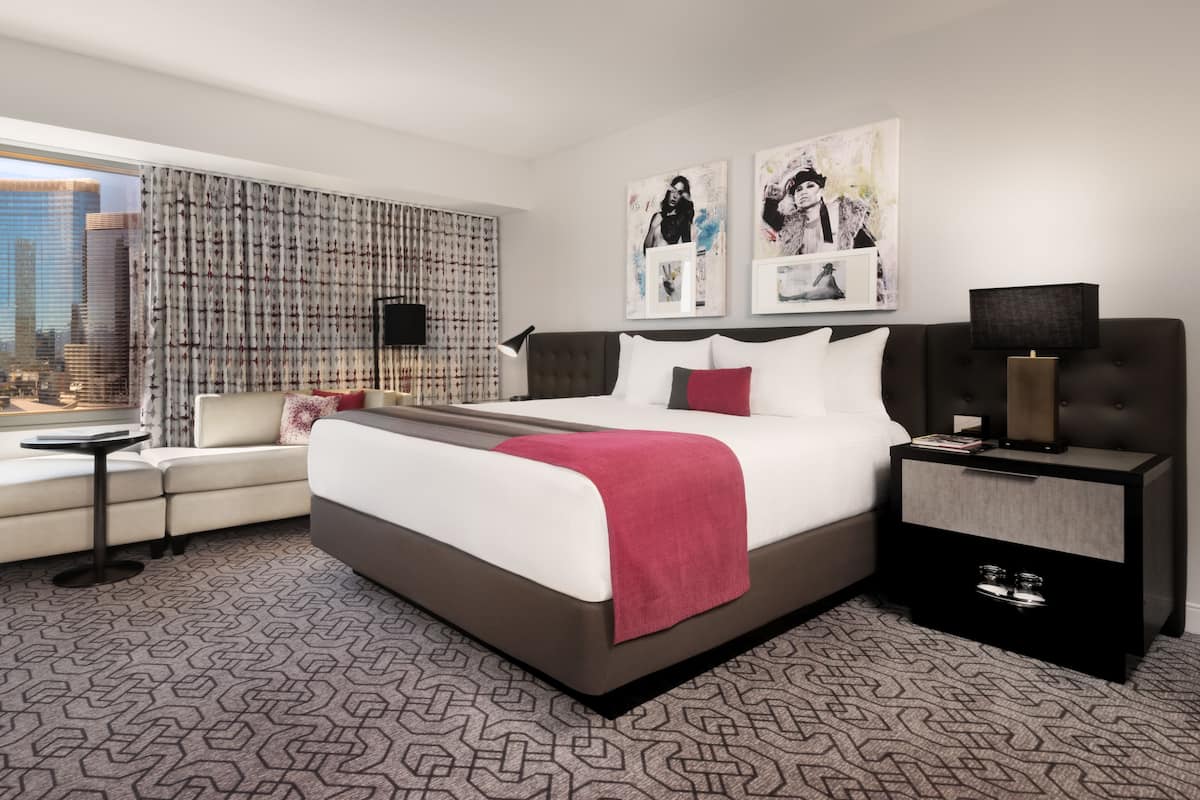 A modern hotel room with a large bed, a seating area, a desk, and a view of the cityscape.
