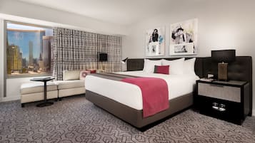 A modern hotel room with a large bed, a seating area, a desk, and a view of the cityscape.