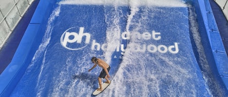 A person surfing on a wave machine with the text "phonet hollywood" and "FLOWRIDER" visible.