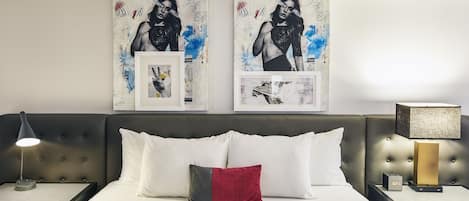 A neatly made bed with white and red pillows, a grey headboard, and a bedside table with a lamp.