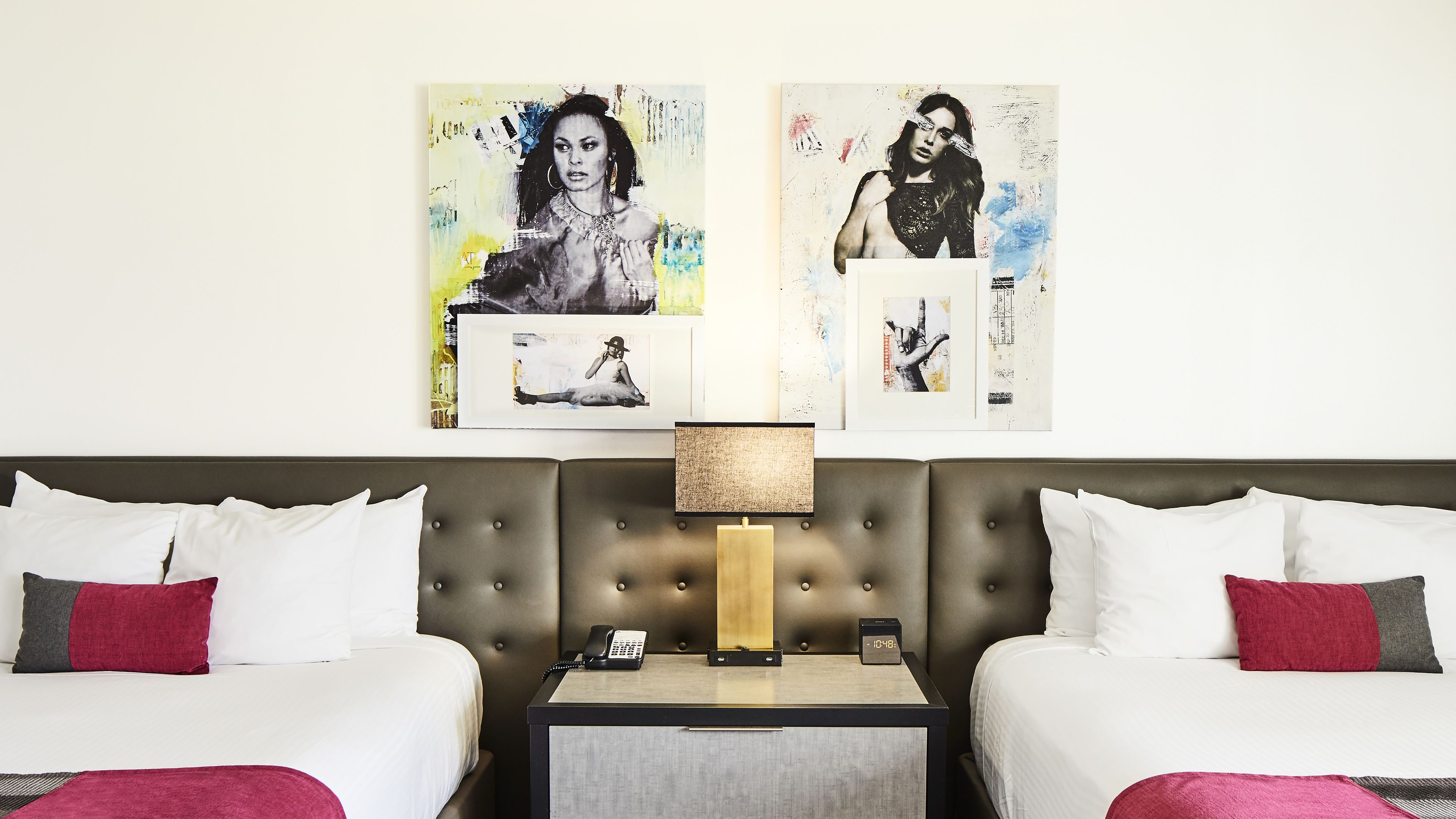 A hotel room with two beds, a nightstand with a lamp, and artwork on the wall.
