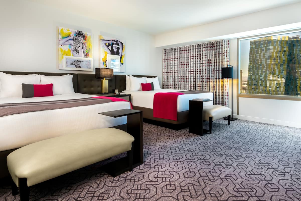 A modern hotel room with a large bed, a smaller bed, a desk, and a chair. There are two paintings on the wall and a window with curtains.