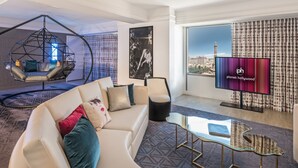 A modern living room with a sofa, a hanging chair, a glass coffee table, and a television displaying 'planet hollywood'. - Planet Hollywood Resort & Casino (Las Vegas)