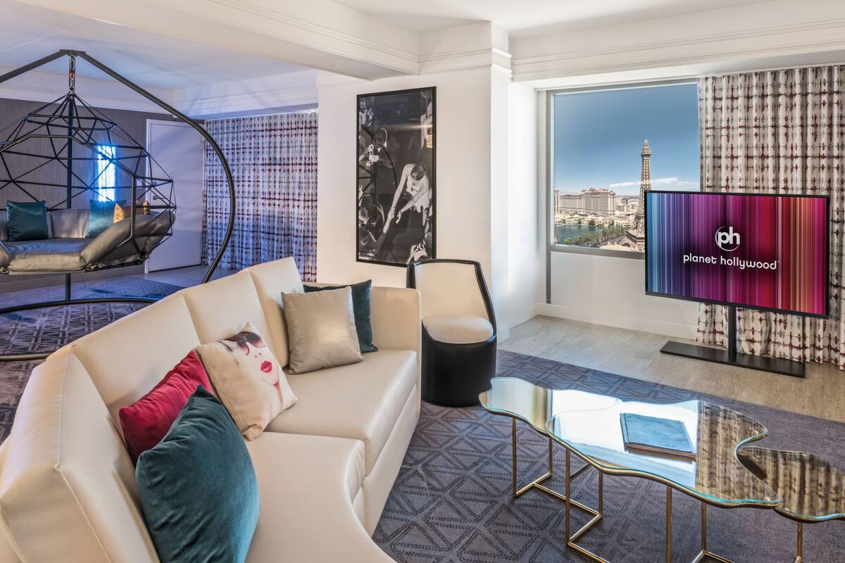A modern living room with a sofa, a hanging chair, a glass coffee table, and a television displaying 'planet hollywood'.