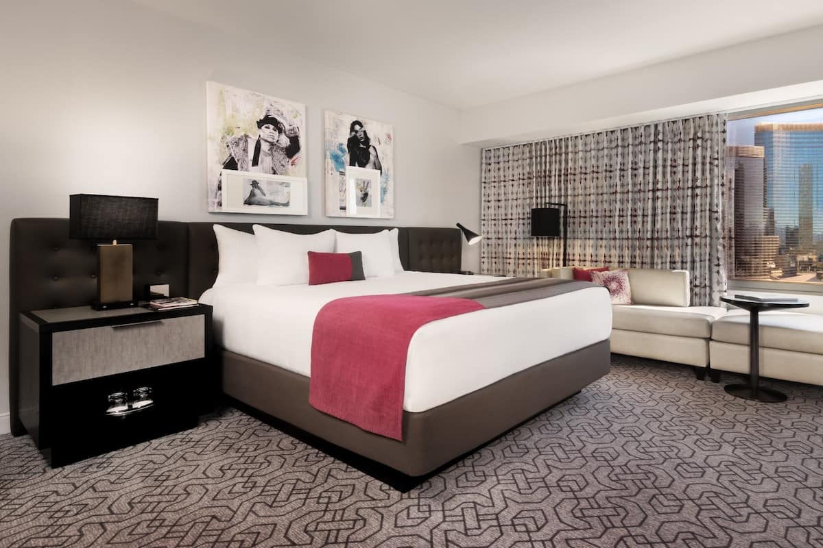 A modern hotel room with a large bed, a sofa, a small table, and a city view.
