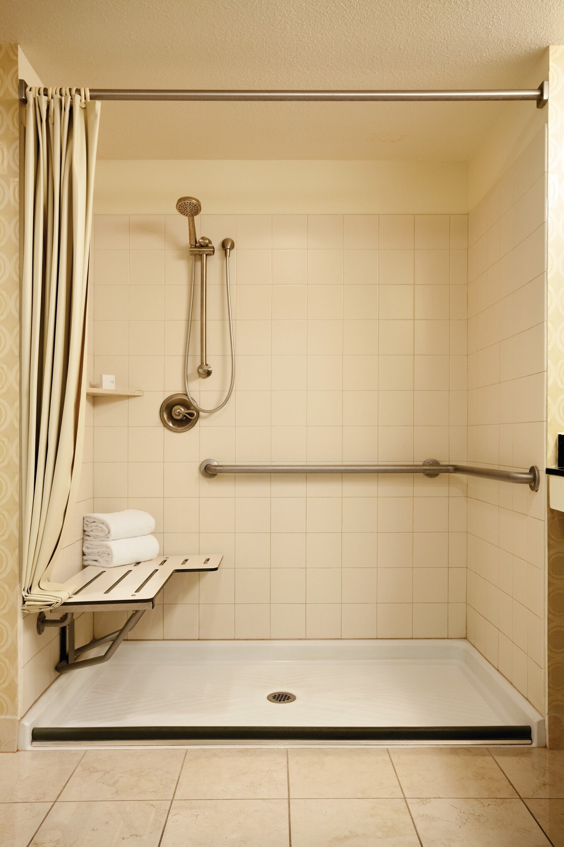 A wheelchair-accessible shower with a grab bar, a towel rack, and a shelf.