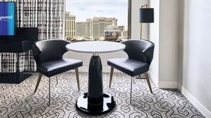 A hotel room with a round table, two chairs, a TV, and a view of a casino building.