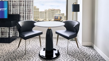 A hotel room with a round dining table, black leather chairs, a black sofa, and a large window offering a cityscape view. at Planet Hollywood Resort & Casino