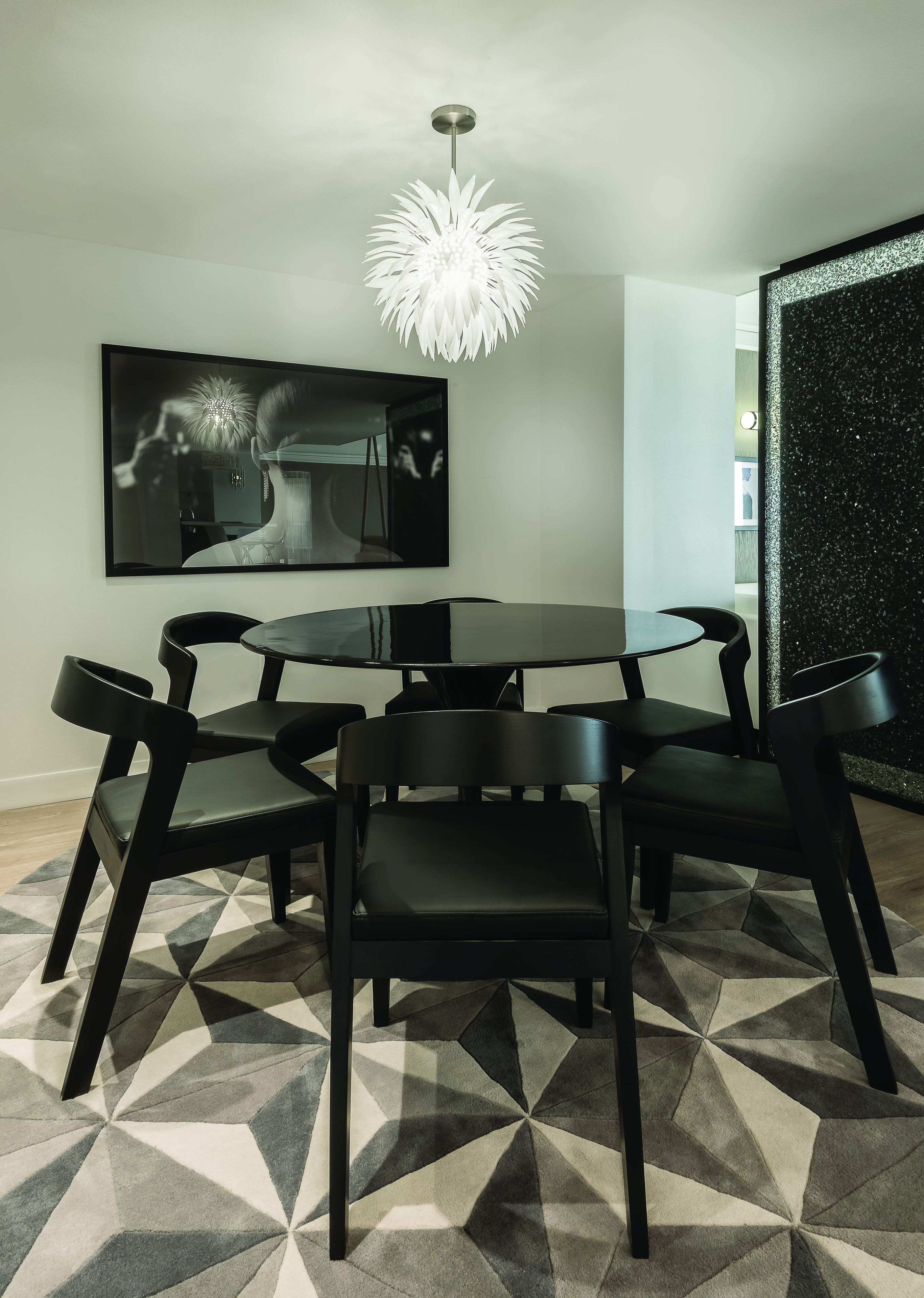 A modern dining area with a round table, six black chairs, and a unique geometric patterned floor.